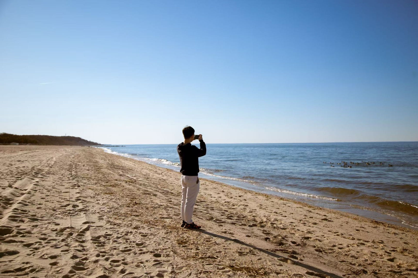 Kai Li standing on a beach beside the water on a clear day.