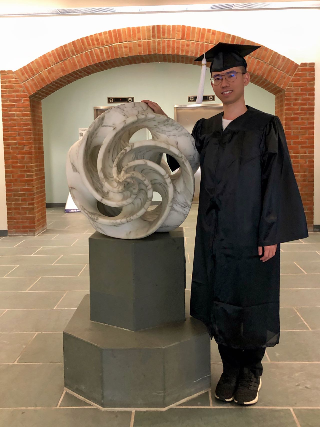 Kai Li in Ohio State graduation regalia outside the Mathematics Tower near the Golden Hour Glass sculpture.