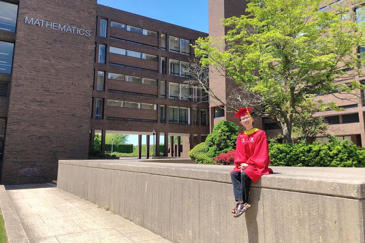 Kai Li in graduation regalia beside the Umbilic Torus sculpture at Stony Brook University.